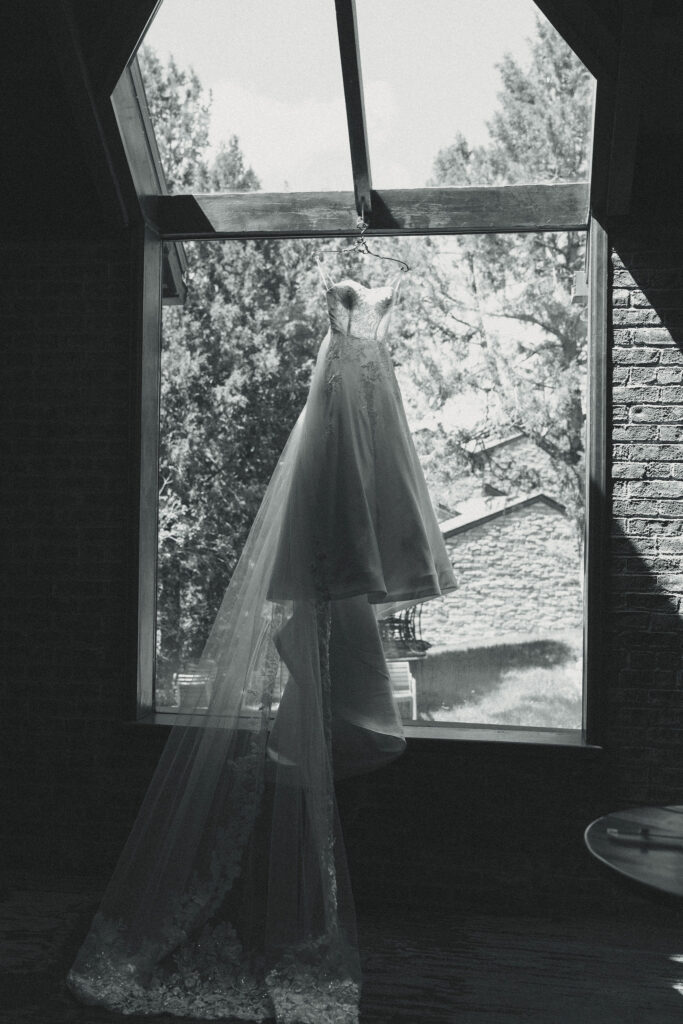 brides dress hangs in a window as she prepares for her stunning wedding day