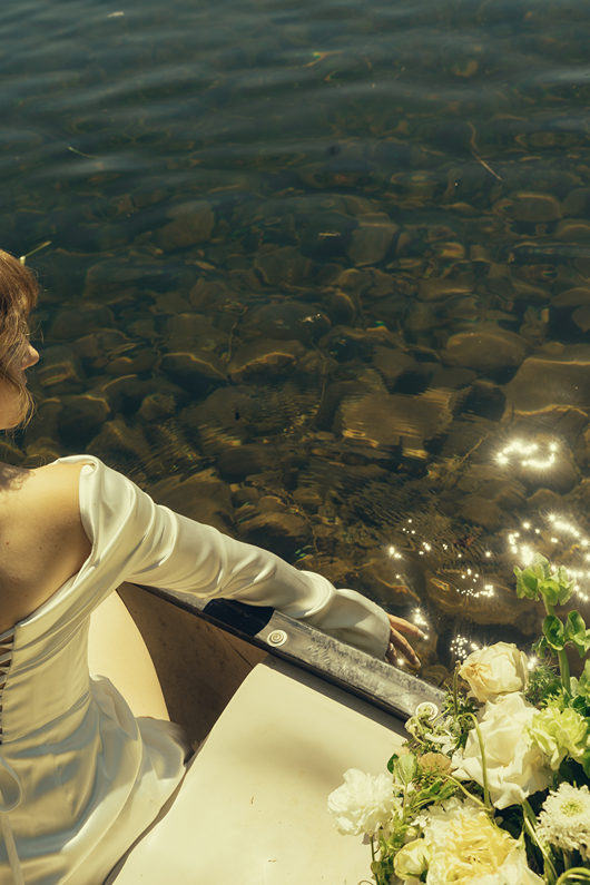 bride poses for a photo on the edge of the canoe with her flowers in the background