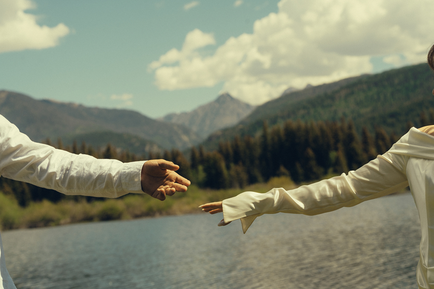 bride and groom reach out for each each other as the lake and mountains sit in the background of their durango colorado wedding photos