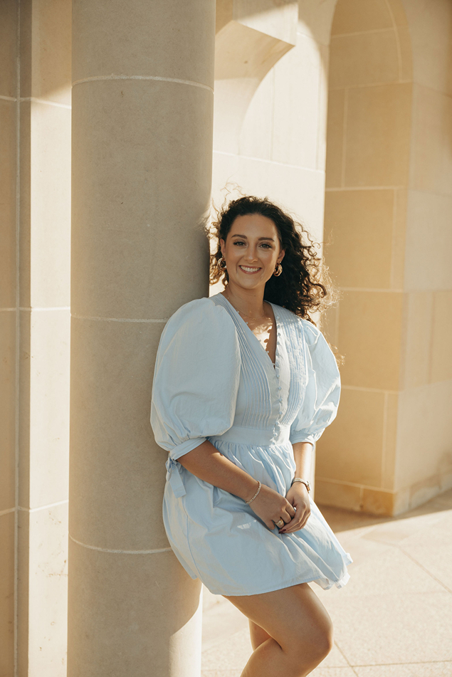 girl in blue dress poses against the building wall during her texas a&m graduation photos