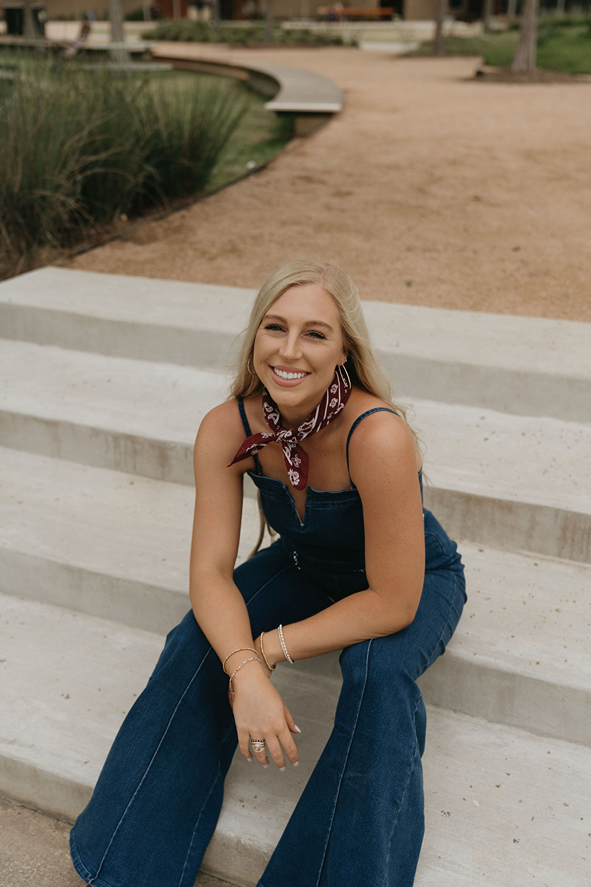 blonde senior sits on the stairs and smiles at the camera