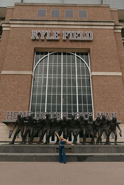 blonde girl in blue jean onesie poses in front of the Kyle Field 12th man statue during her texas a&m graduation photos
