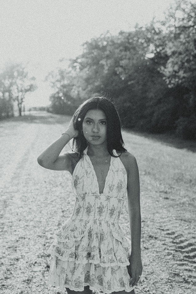 black and white photo of a girl walking on a road adjusting her hair during her session captured by Sasha Takes Pictures a Texas senior photographer 