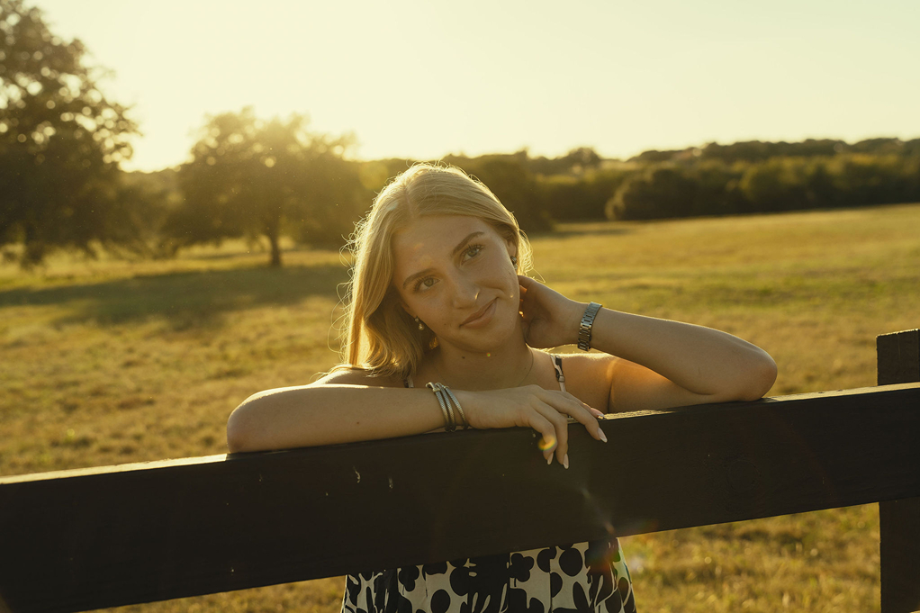 senior poses on a fence during golden hour senior photos