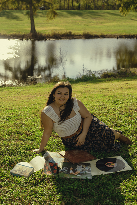 girl sits with vinyls and a book by the pond during her mini senior session