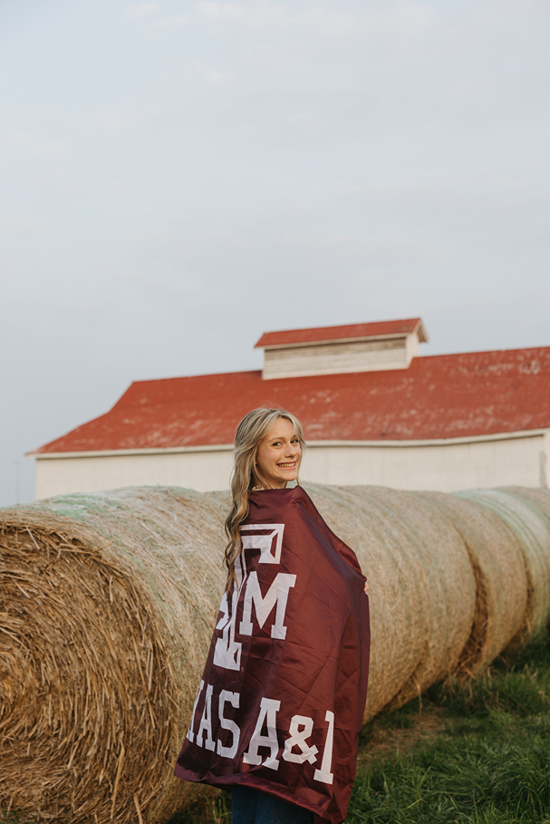 senior poses on a farm with a Texas A&M Flag