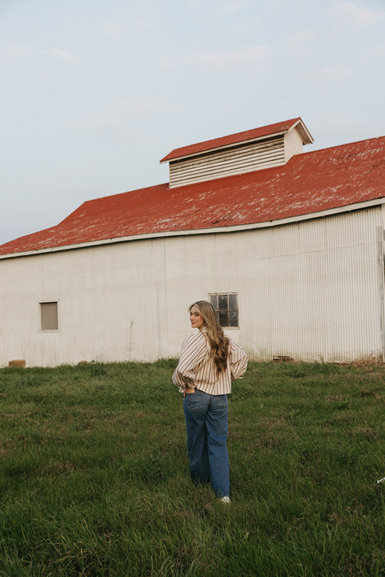 senior walks towards a barn during her unique senior photoshoot on a farm