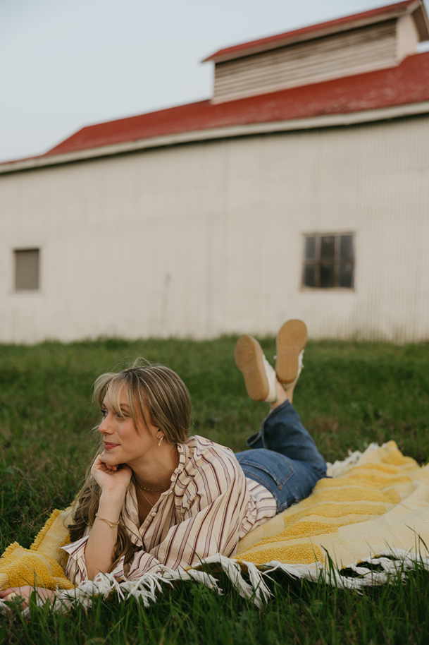 senior poses on a farm lying on a blanket