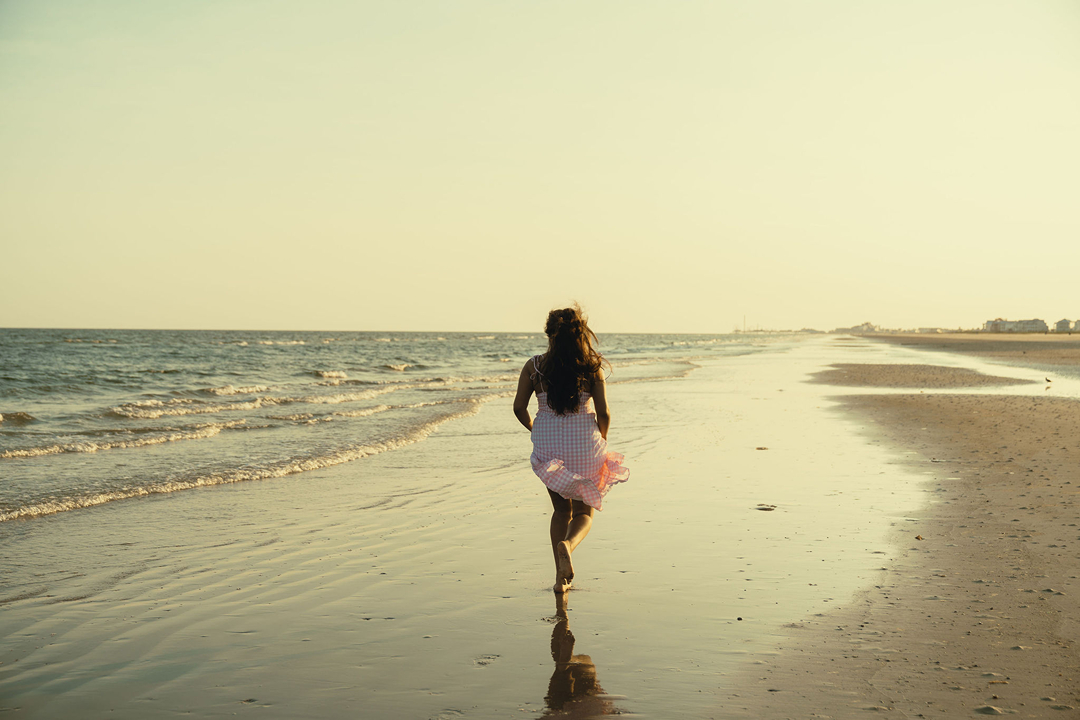 senior runs down the beach as the waves lap the shore beside her