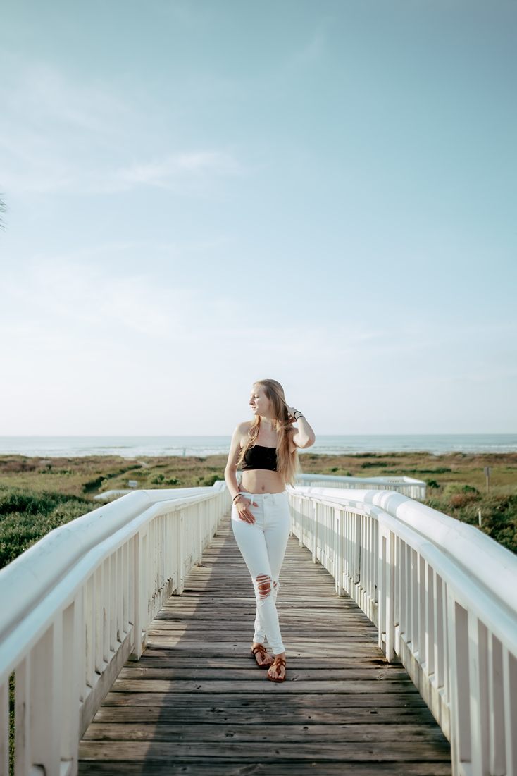 senior poses on the boardwalk leading down to the Galveston beach
